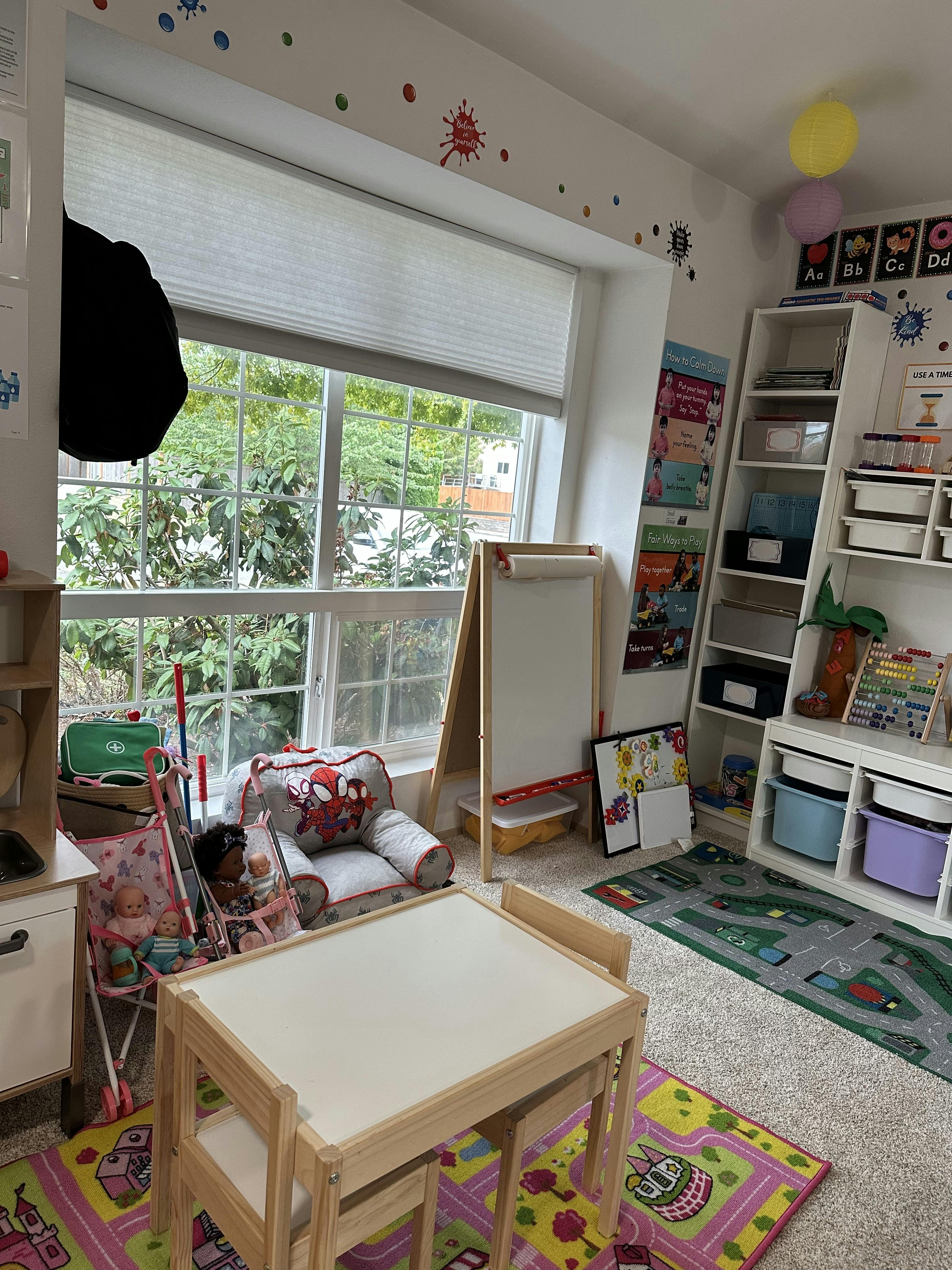 A child play area with a small table, chairs, toy strollers, and storage bins