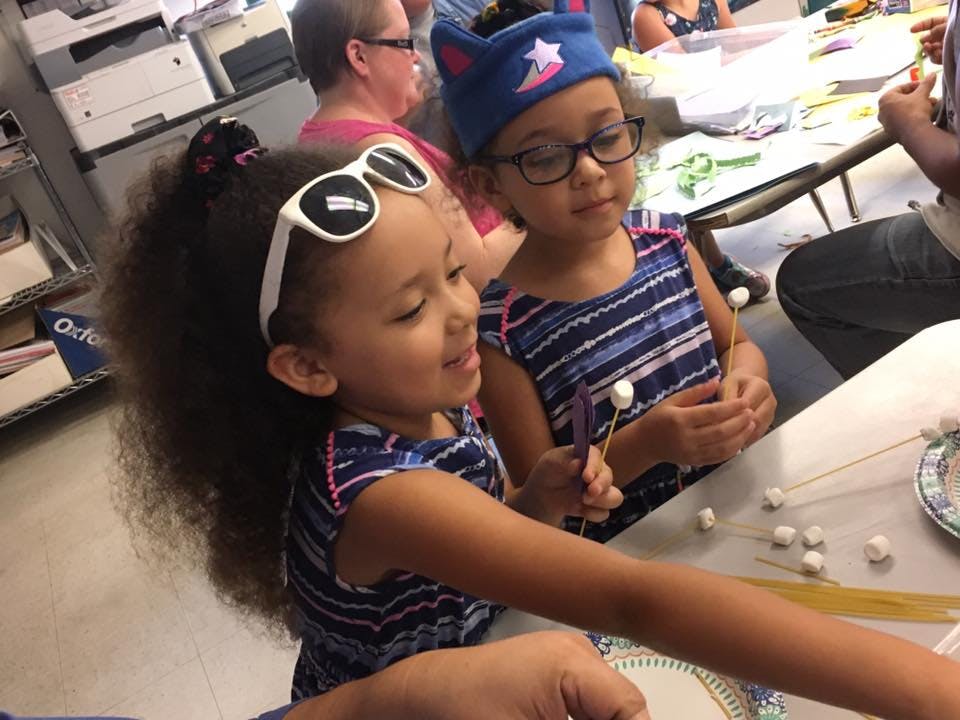 Two children at a table with marshmallows and sticks