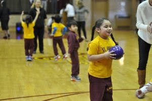 Child holding a purple ball on a gym floor