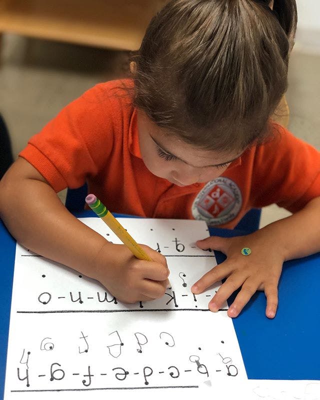Child writing letters on a worksheet with a pencil