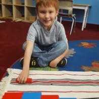 Child sitting on floor with a rug, moving a red block