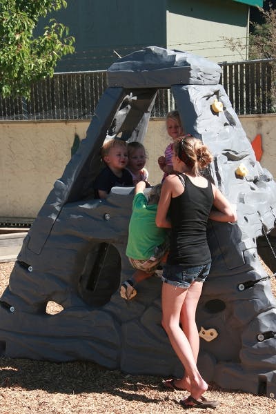 Person standing next to children on a playground climbing structure