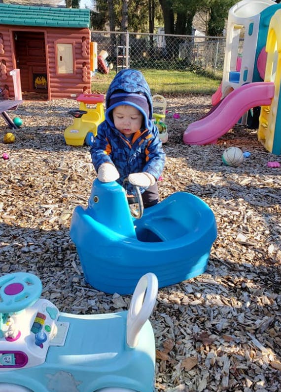 Child in a blue coat playing with a blue toy boat on a playground