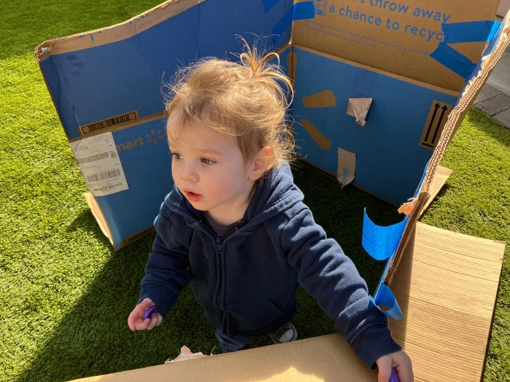 Child in a cardboard box fort on grass