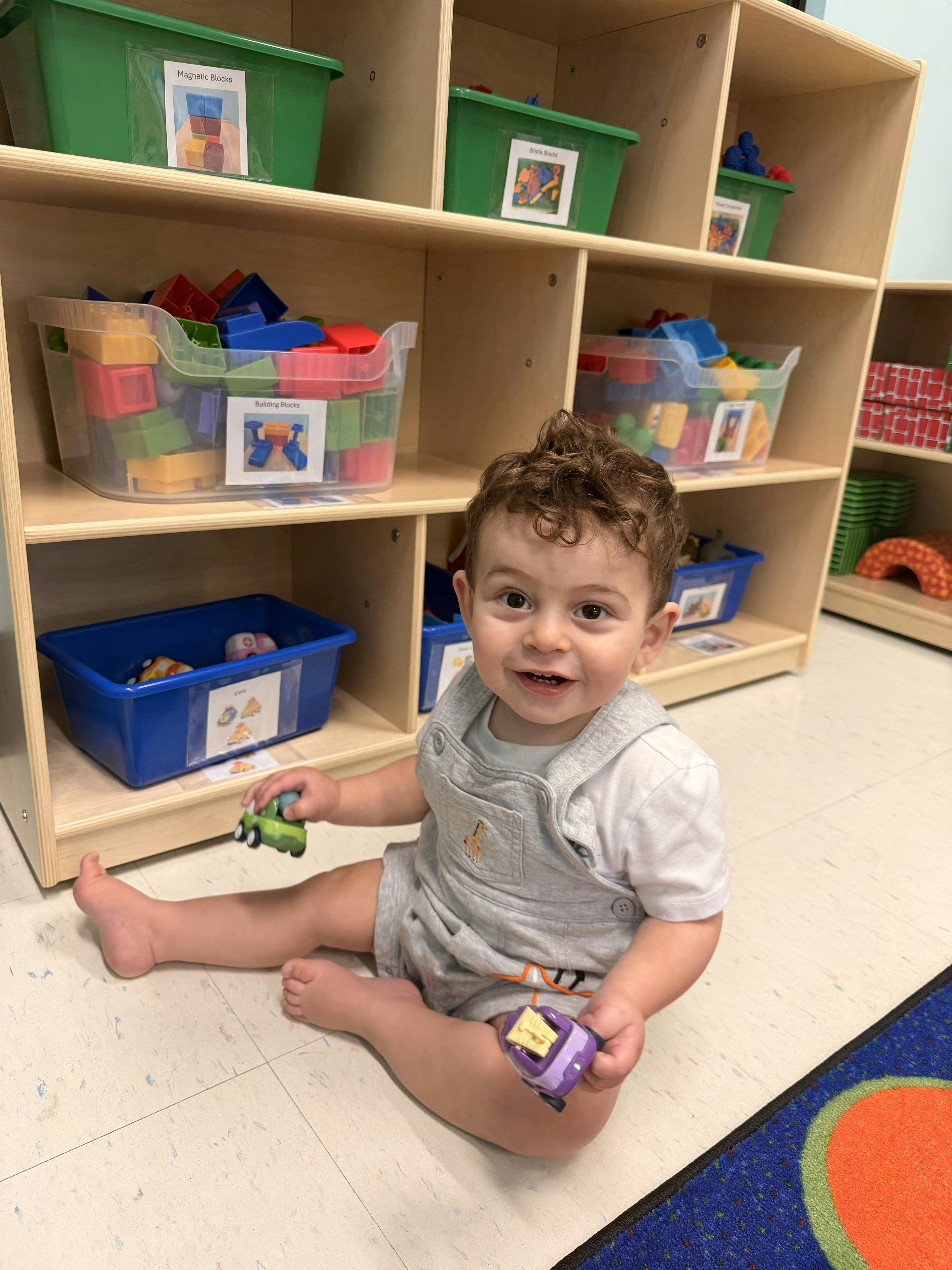 Child sitting on a classroom floor playing with small toy cars