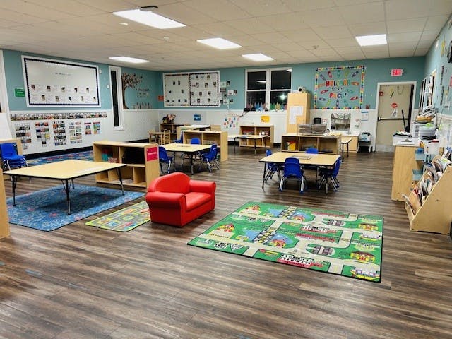 empty preschool classroom with tables, chairs, and colorful rugs