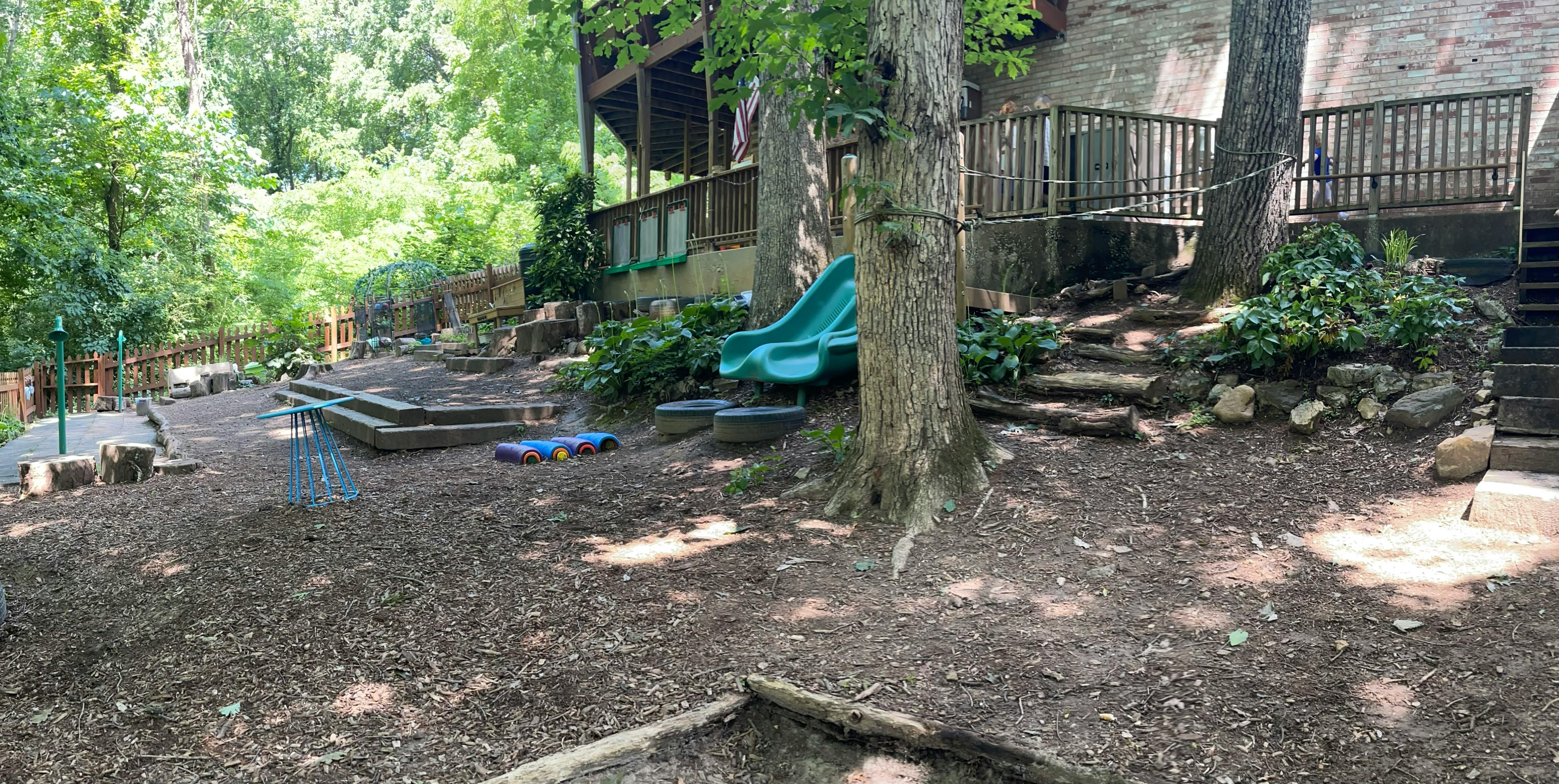 Outdoor play area with a green slide, tires, and small toys on wood chips
