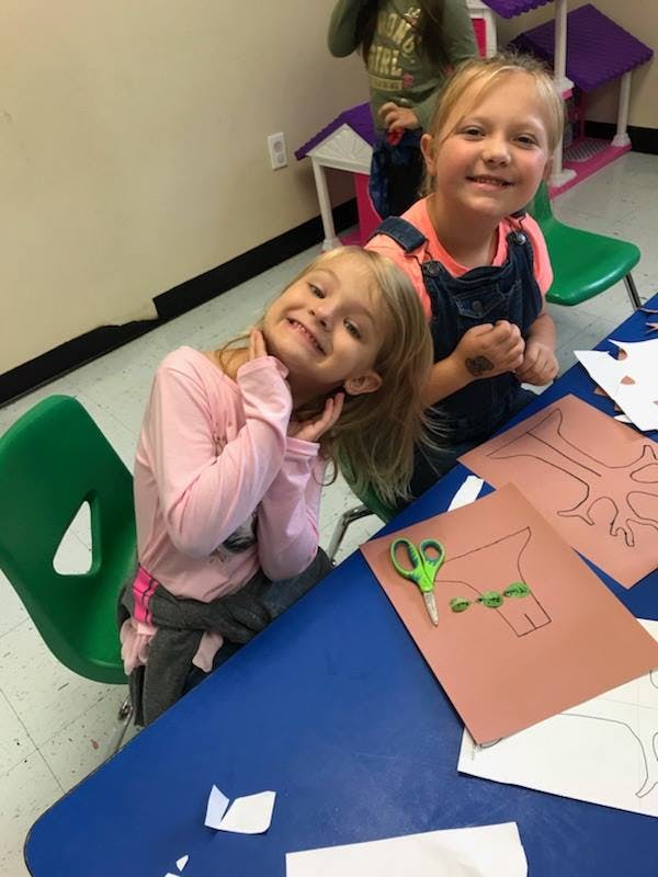 Two children at a table with paper cutouts and scissors
