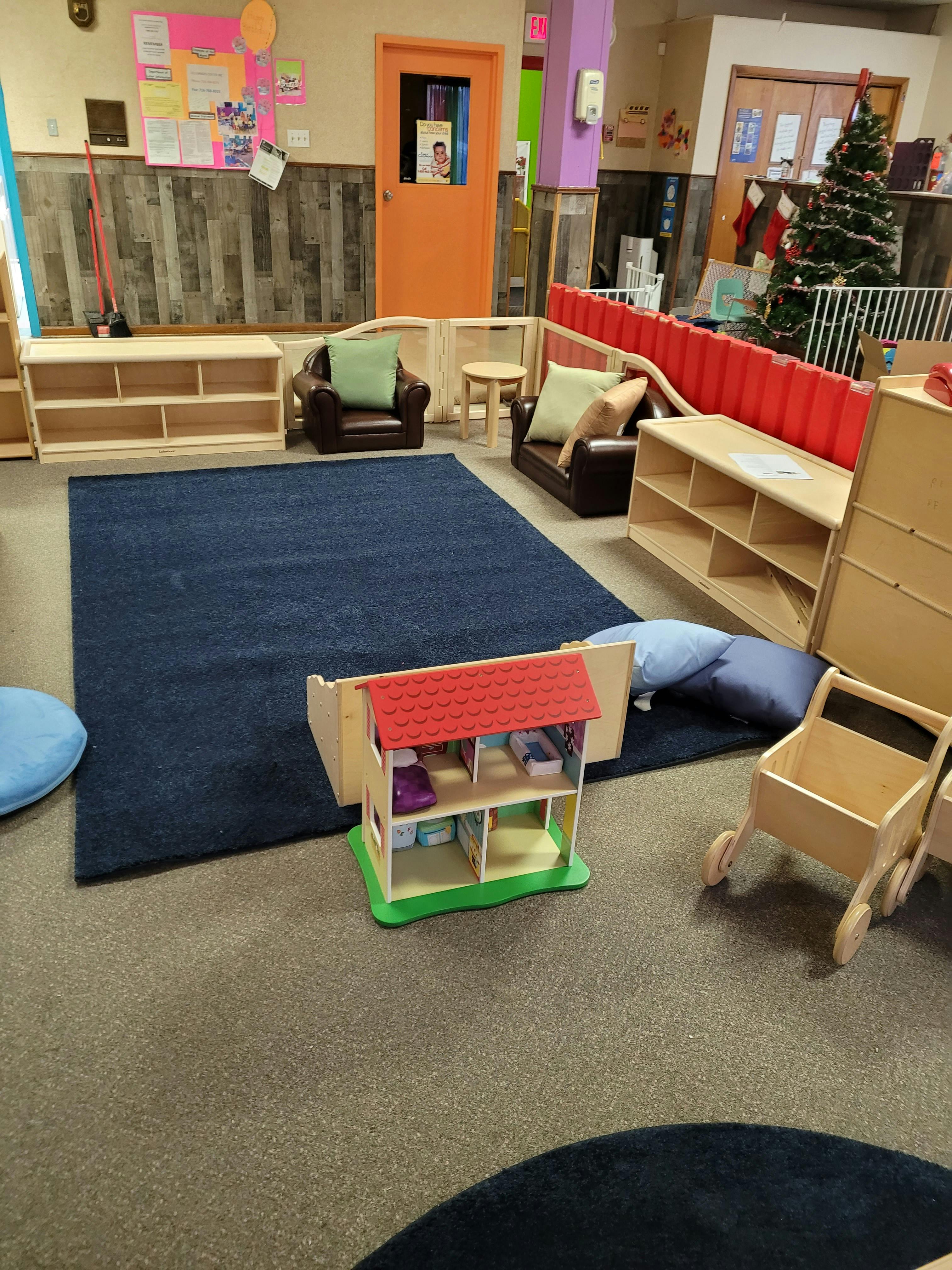 Playroom with a blue rug, small chairs, shelves, and a dollhouse