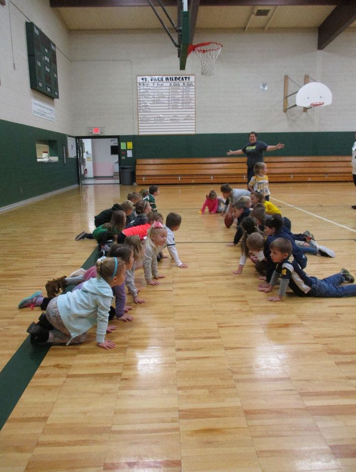 Children crawling on a gym floor with an adult standing in the background