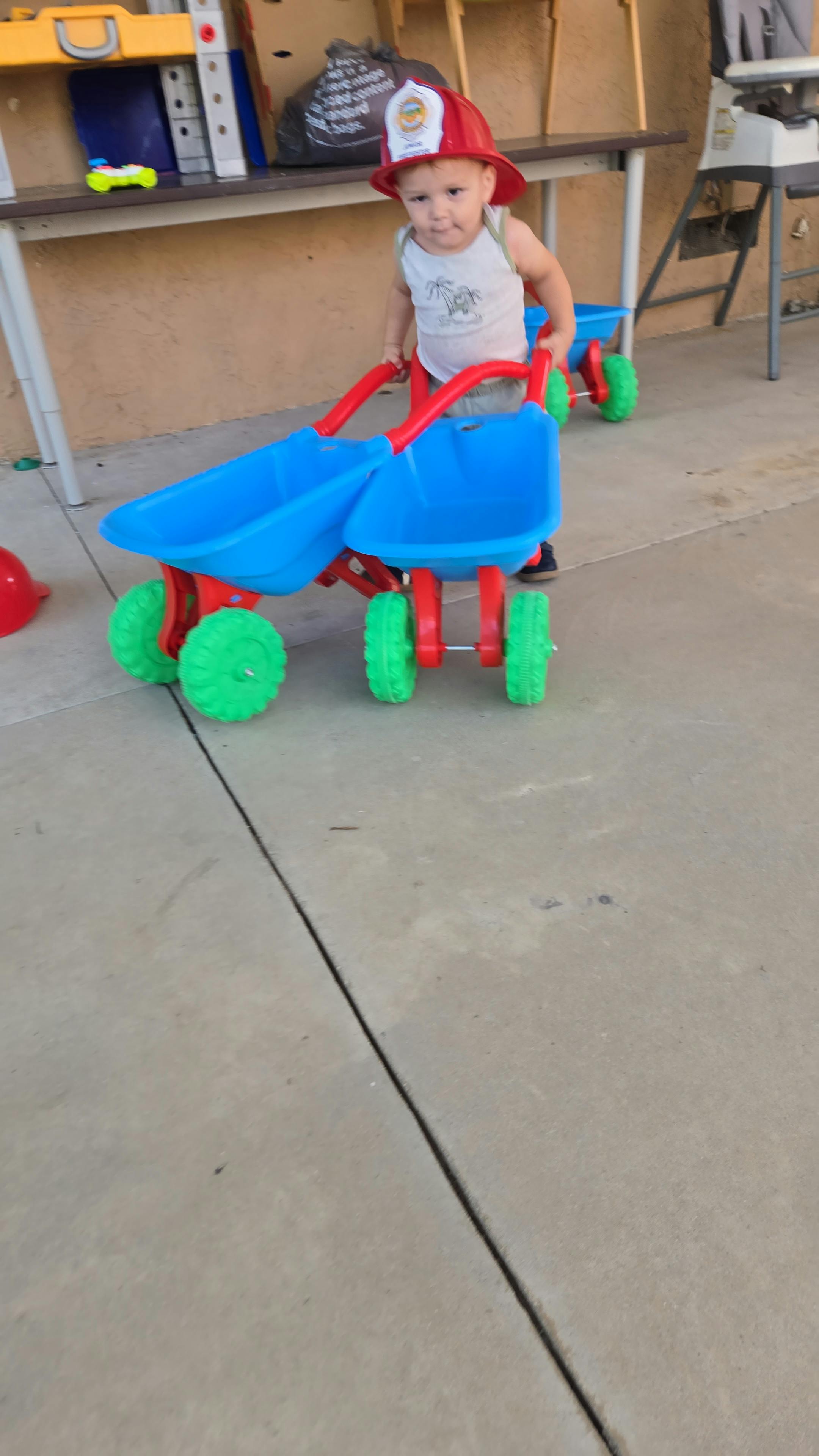 Child wearing a toy helmet pushing a plastic toy cart
