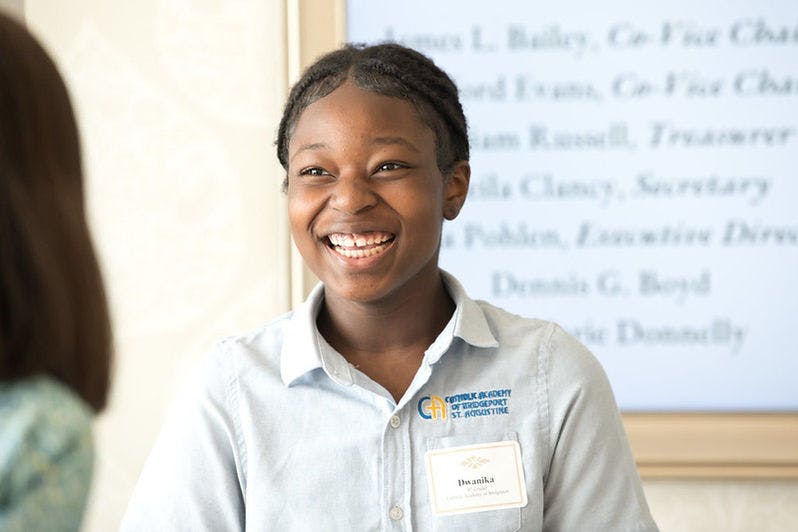 Child in a light blue uniform shirt with a name tag, smiling
