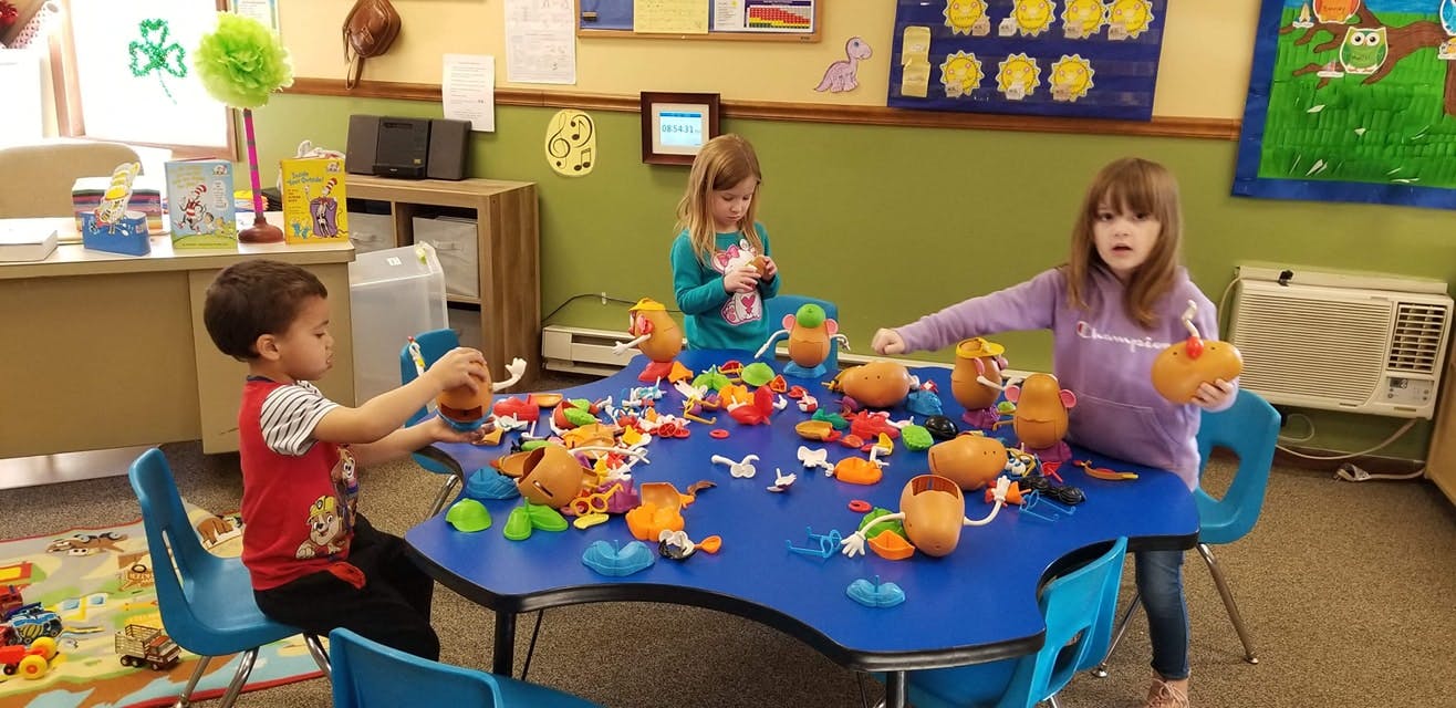 Three children playing with toys at a blue table in a classroom