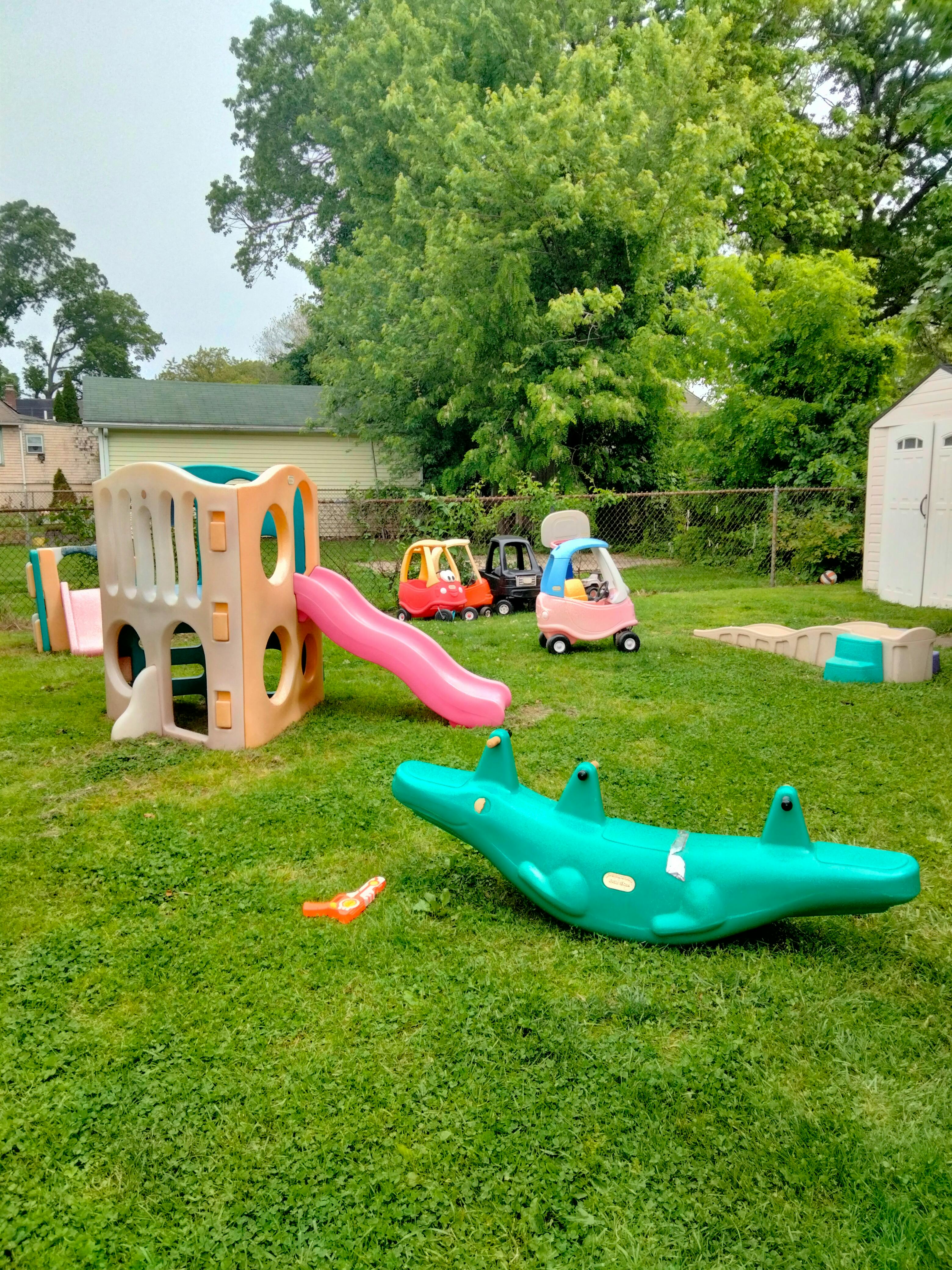 Outdoor playground with slide, ride-on toys, and a green seesaw