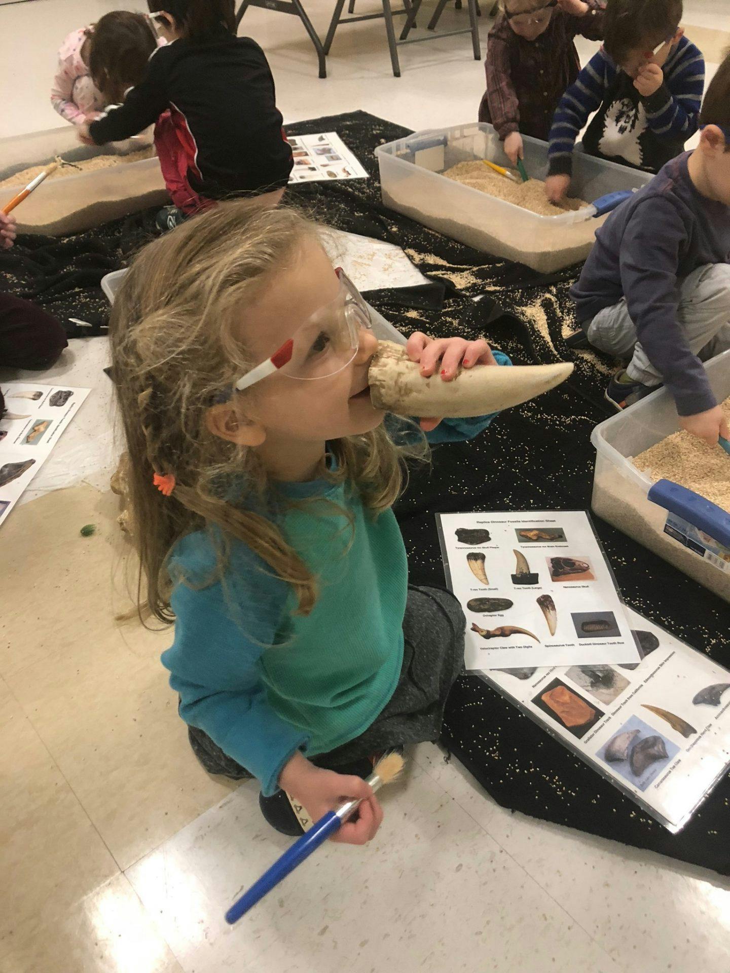 Child wearing safety glasses holding a large tooth replica