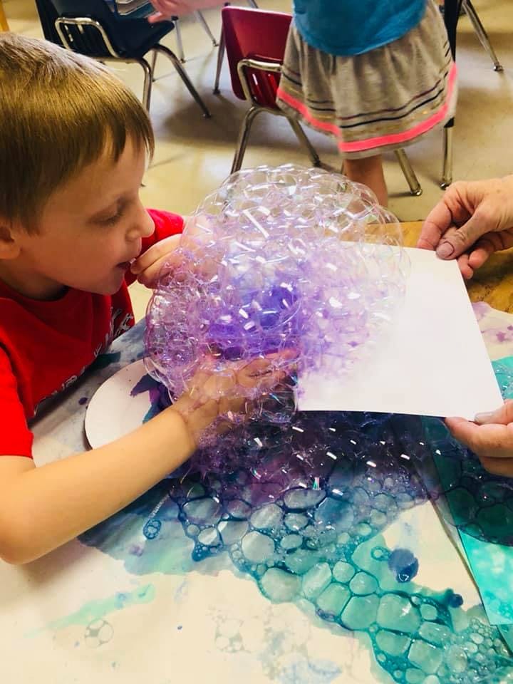 Child blowing bubbles onto paper held by an adult