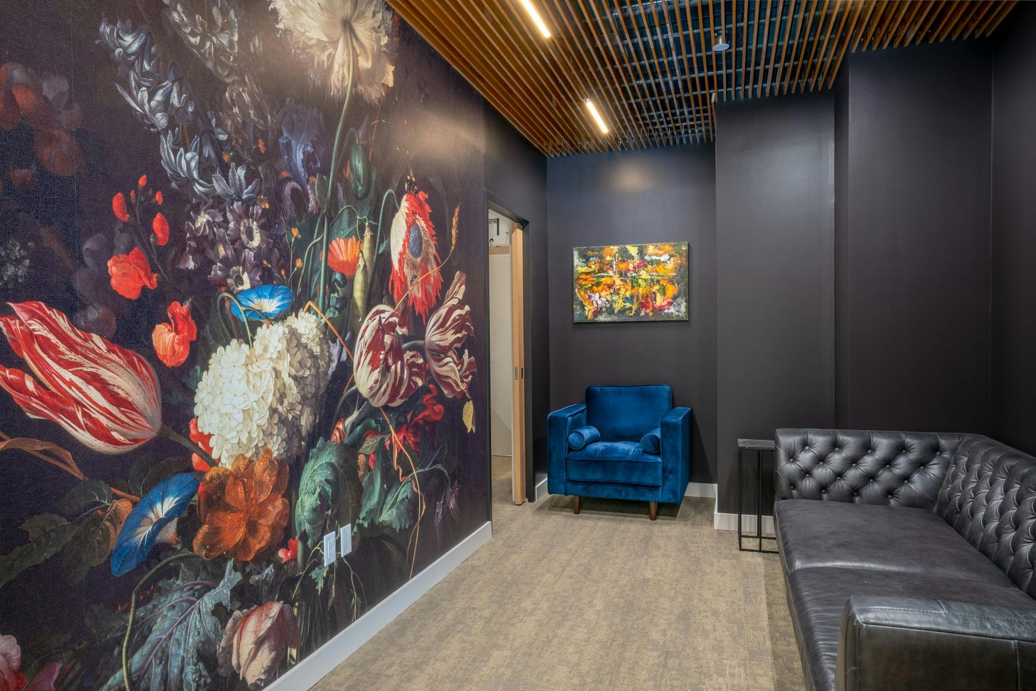 Lounge area with floral wallpaper, blue armchair, and black sofa