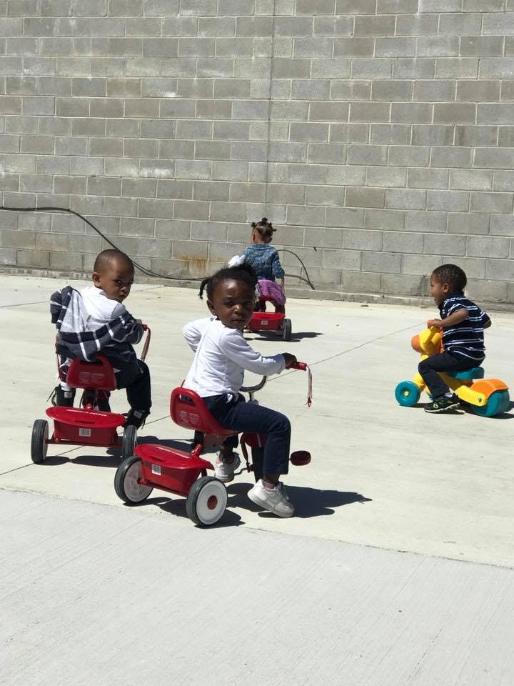Three children riding tricycles on pavement