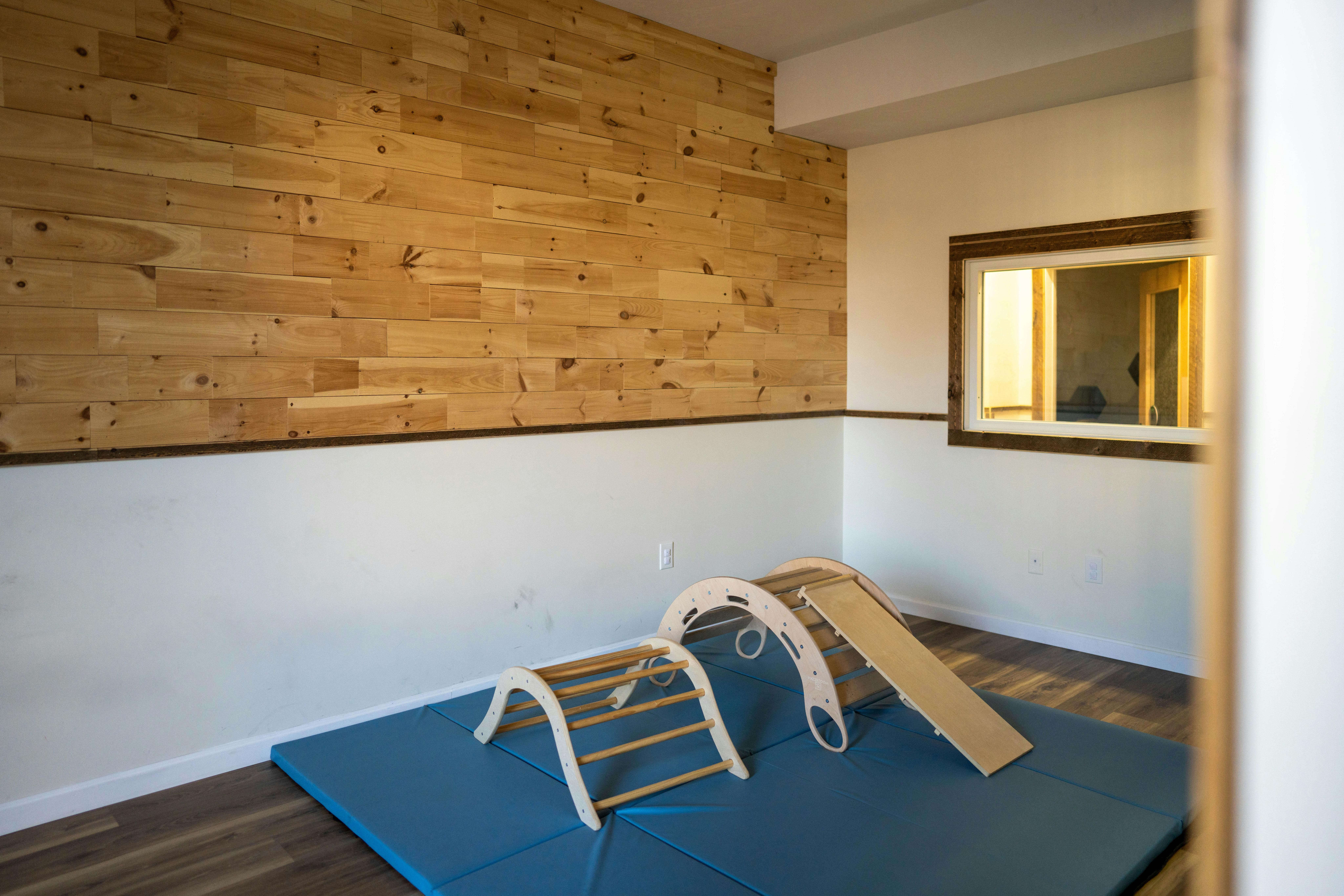 Indoor play area with wooden climbing structures on blue mats
