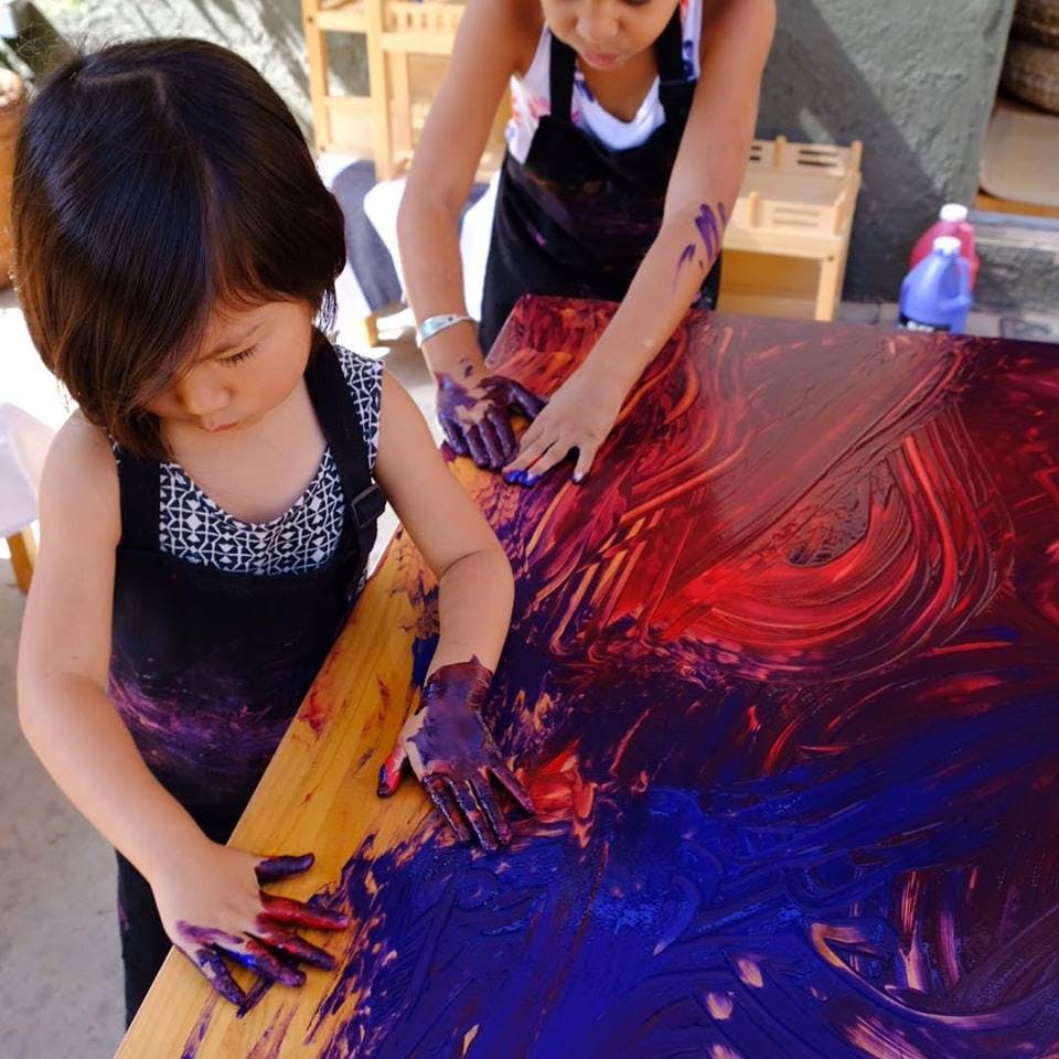 Two children finger painting with red and blue paint on a table