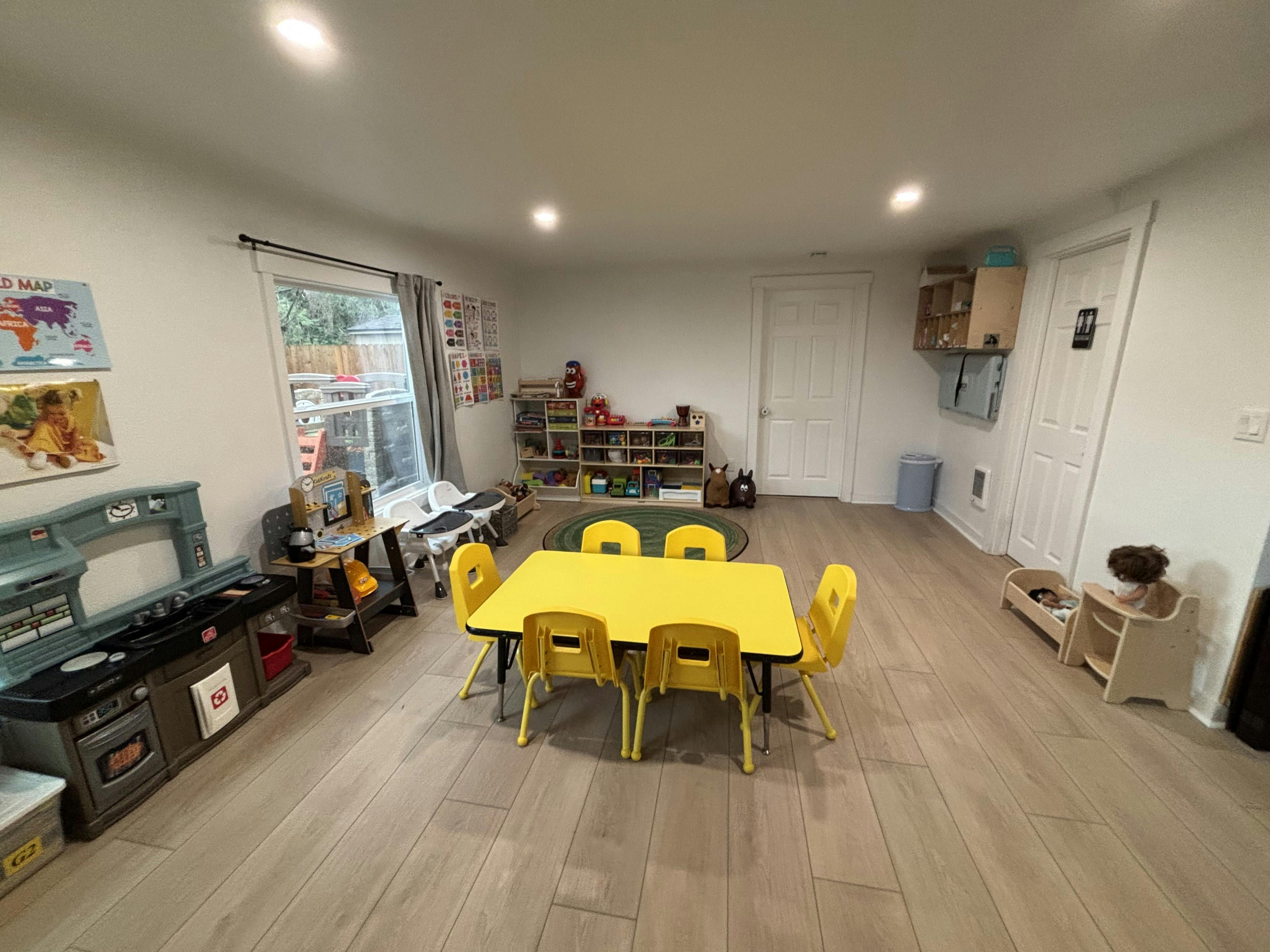 A classroom with a yellow table and chairs, toys, and learning posters