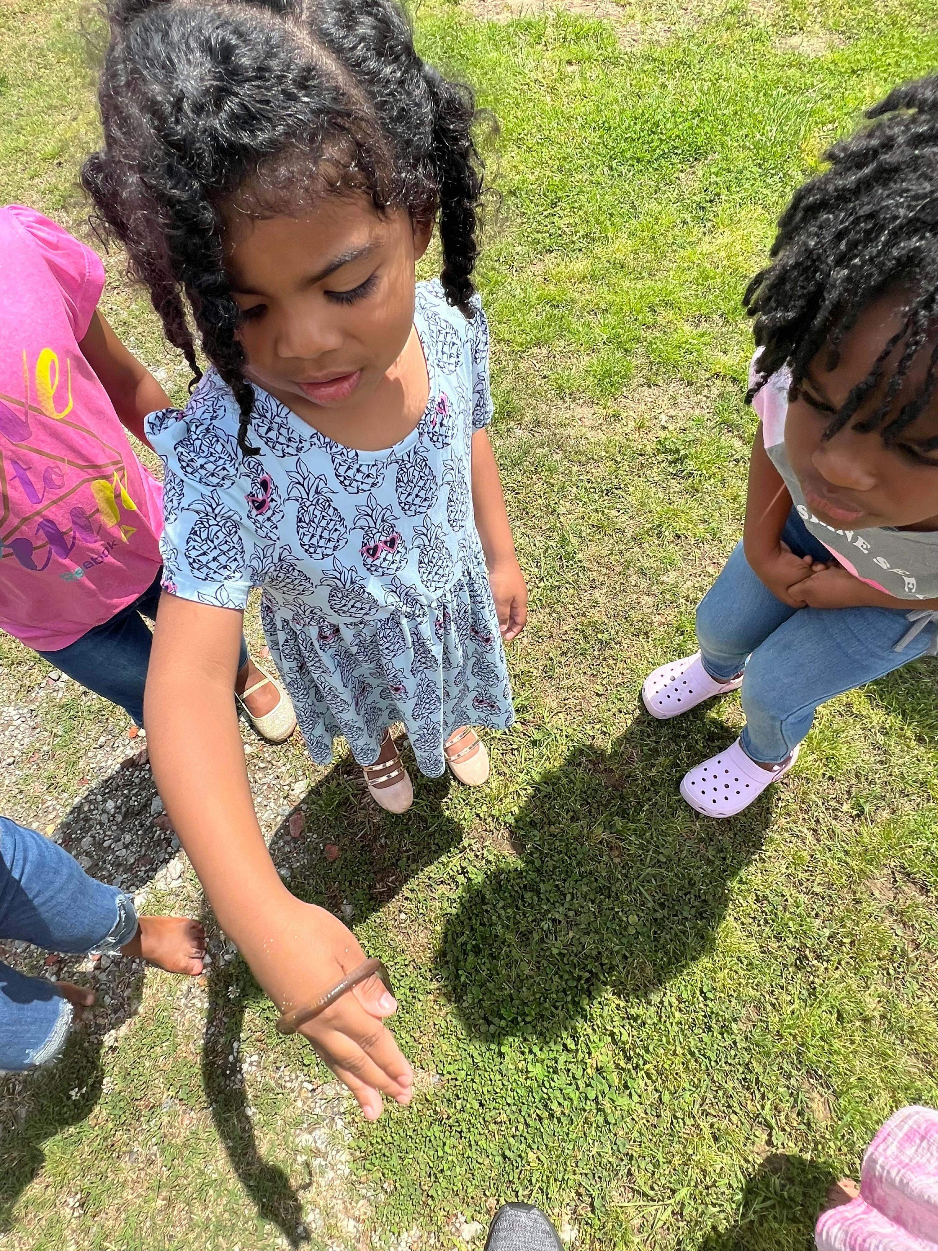 Child in a dress reaching down to the grass with other children around