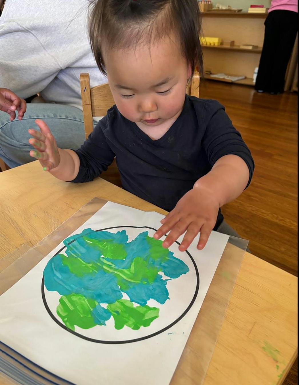 Child finger painting a blue and green circle on a table