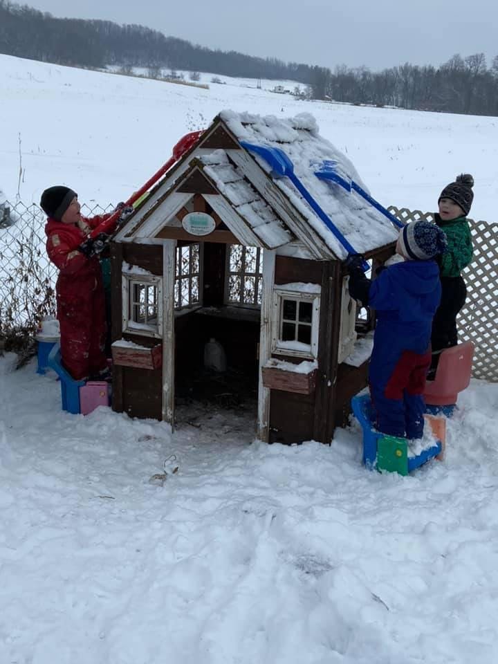 Children shoveling snow off a playhouse roof