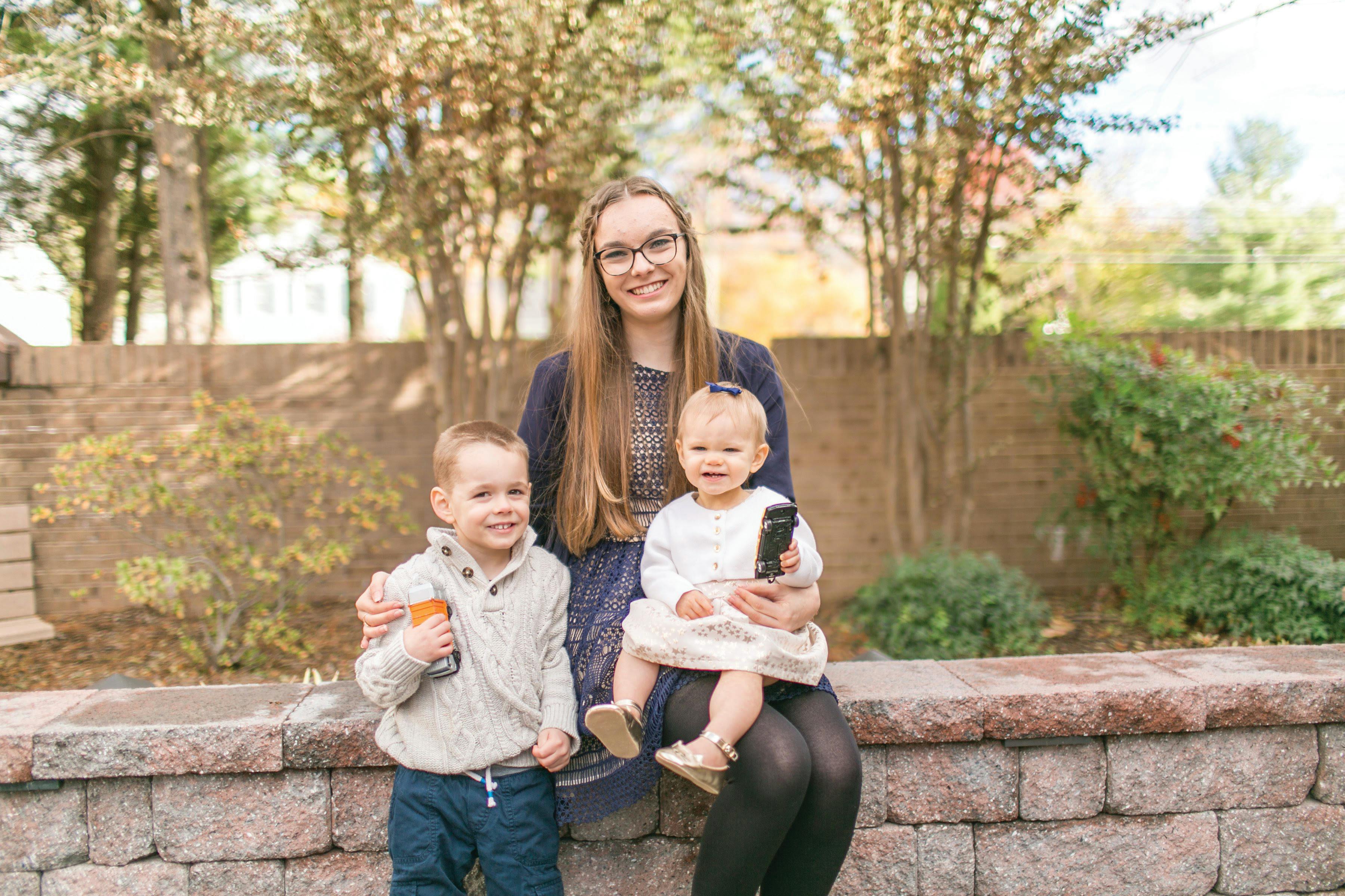 Person with glasses holding a child, another child standing next to them