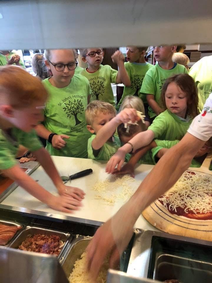 Children making pizza, adding cheese to the dough
