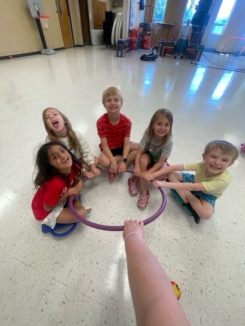 Group of children sitting on the floor in a circle holding a hula hoop