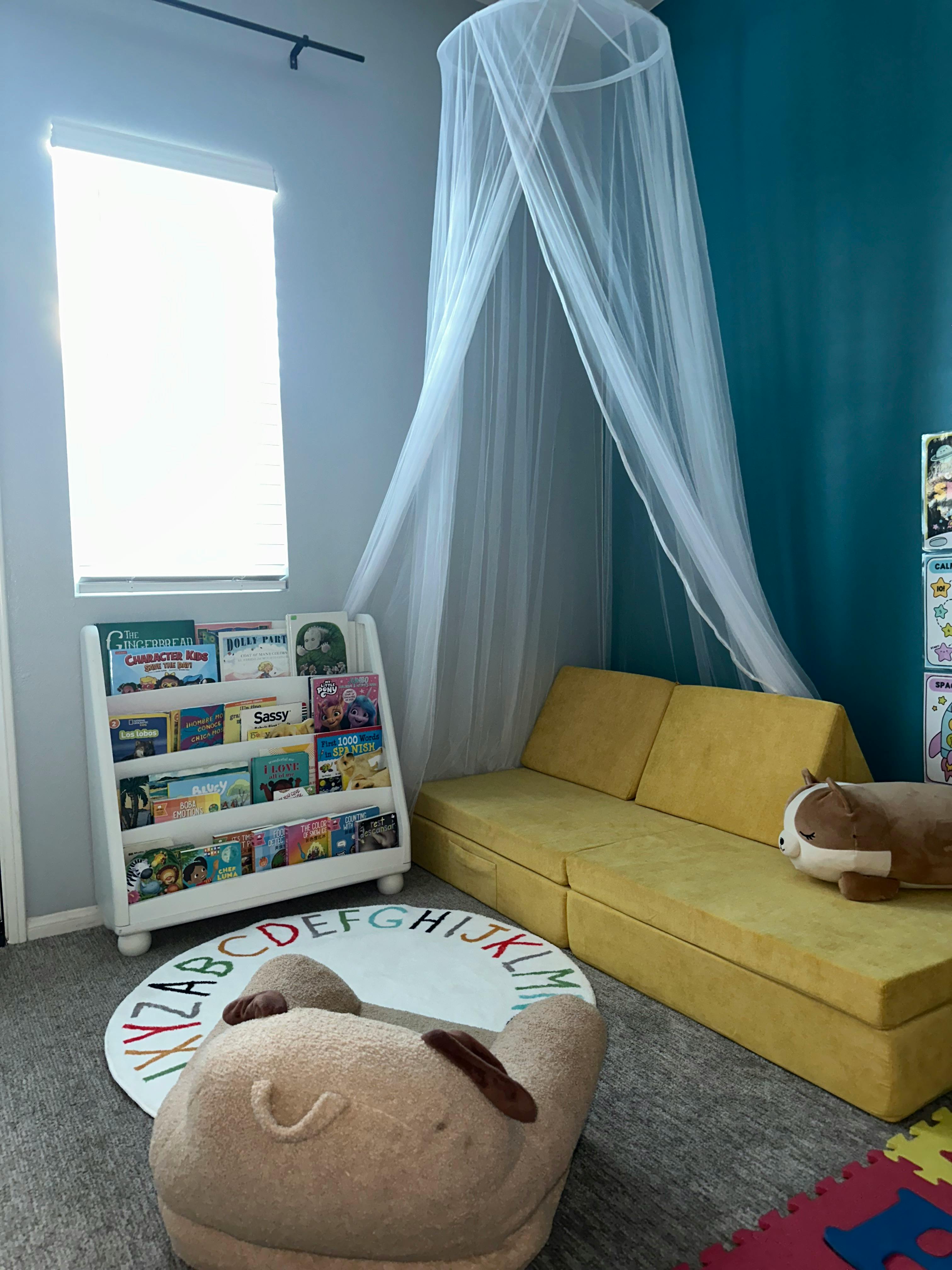Playroom with a modular couch, book rack, alphabet rug, and ceiling canopy