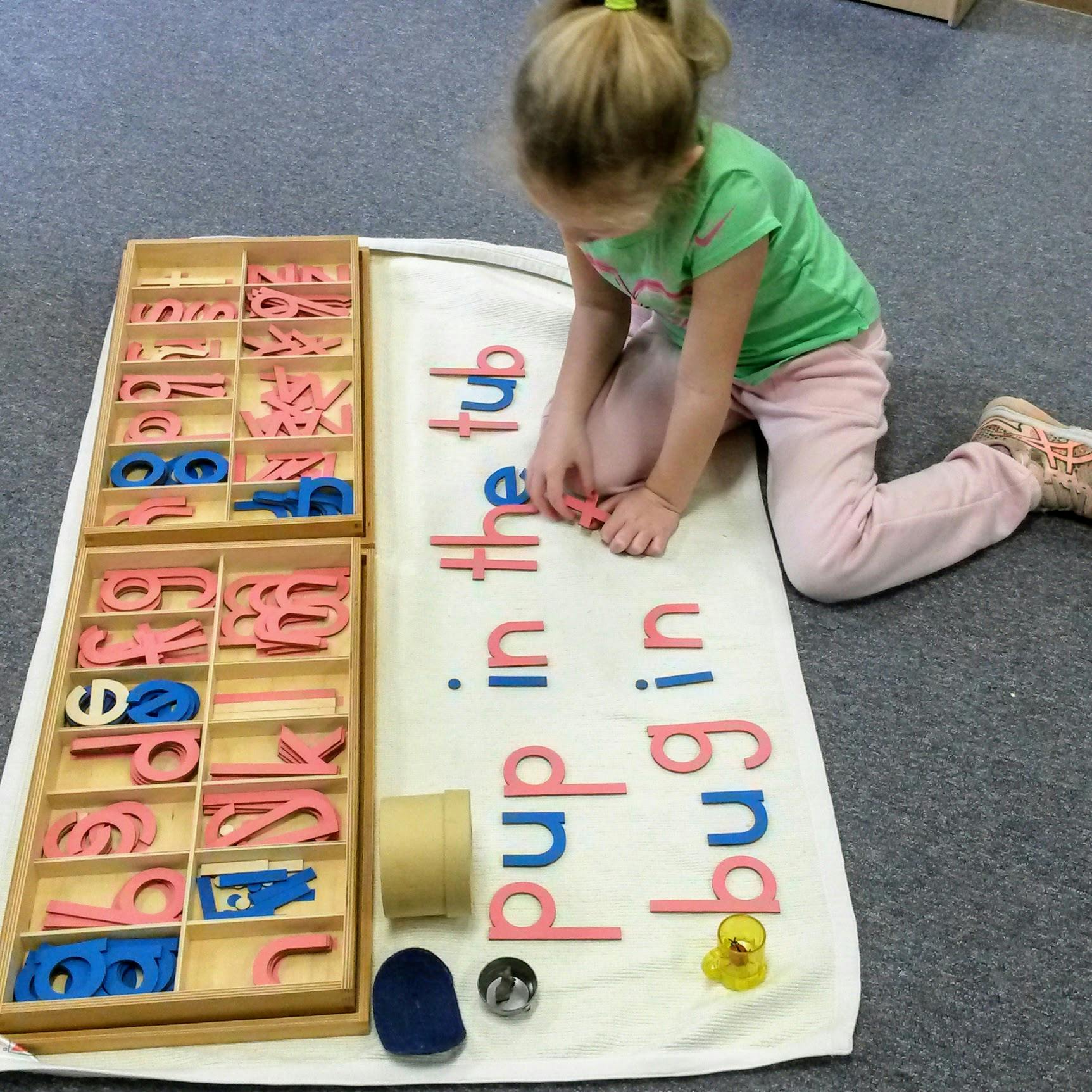 Child kneeling on floor, arranging letter tiles on a mat