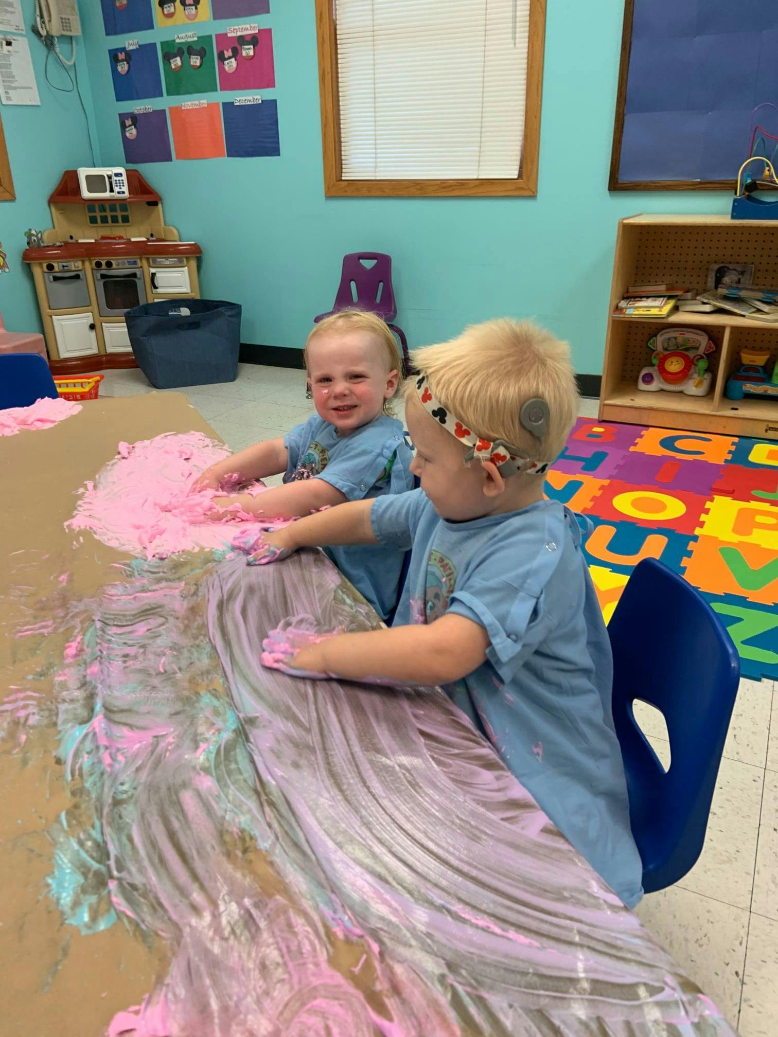 Two children playing with pink and blue paint on a table