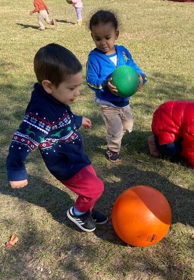 Child kicking an orange ball while another child holds a green ball
