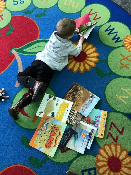 Child lying on a colorful alphabet rug, looking at a book