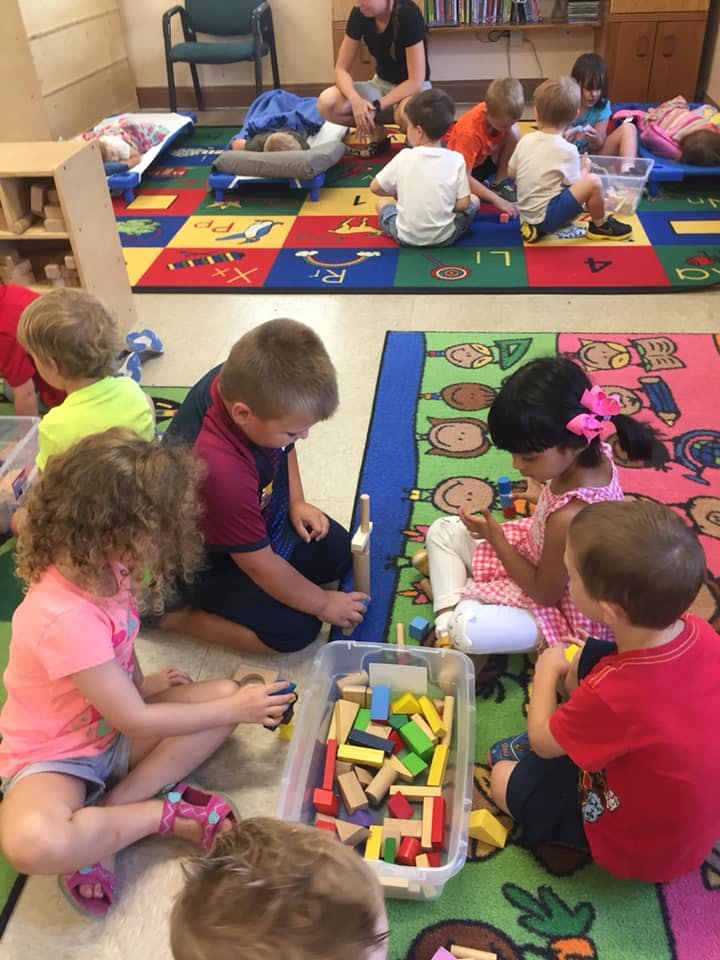 Children playing with blocks on a colorful rug in a classroom
