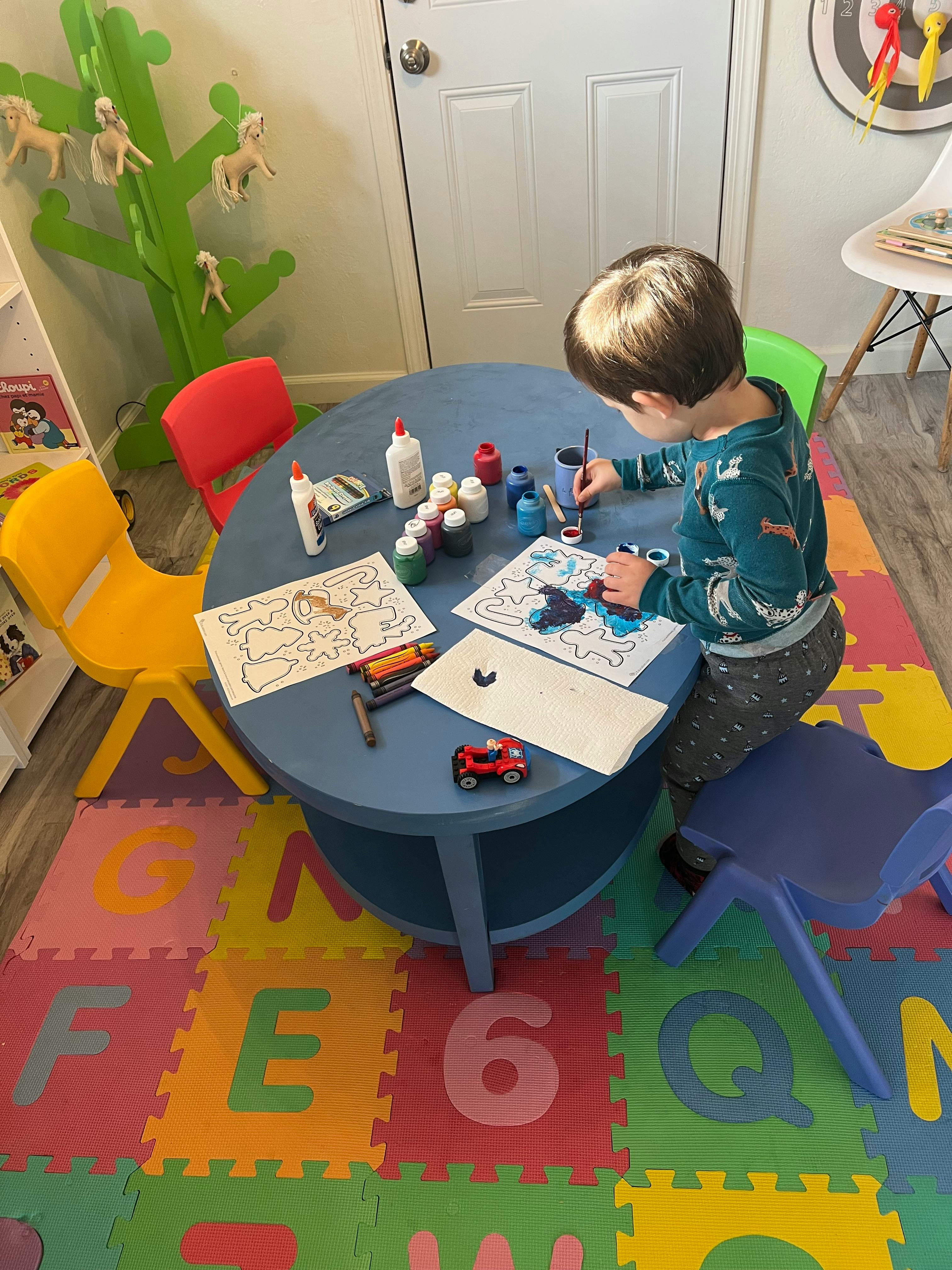Child painting at a table in a room with alphabet floor mats