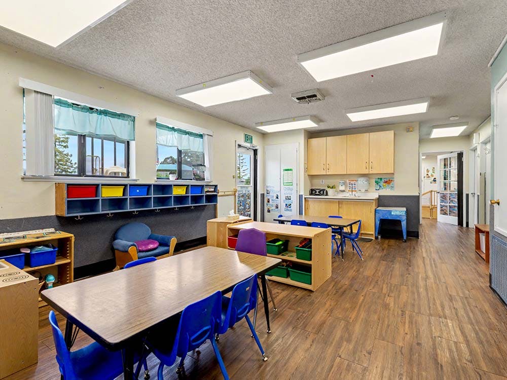 Classroom with tables, blue chairs, cubbies, and windows