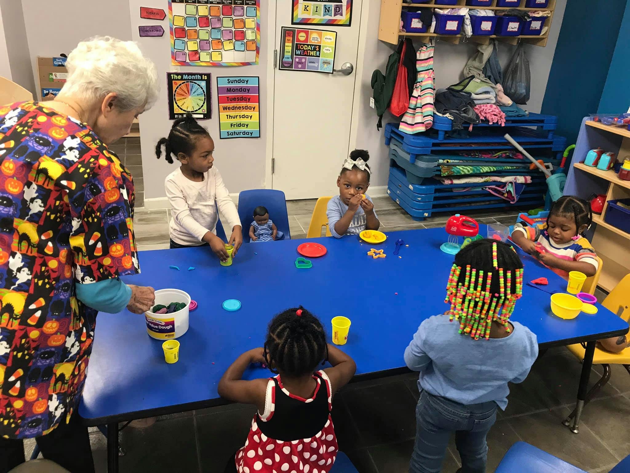 Adult and multiple children around a blue table with play items