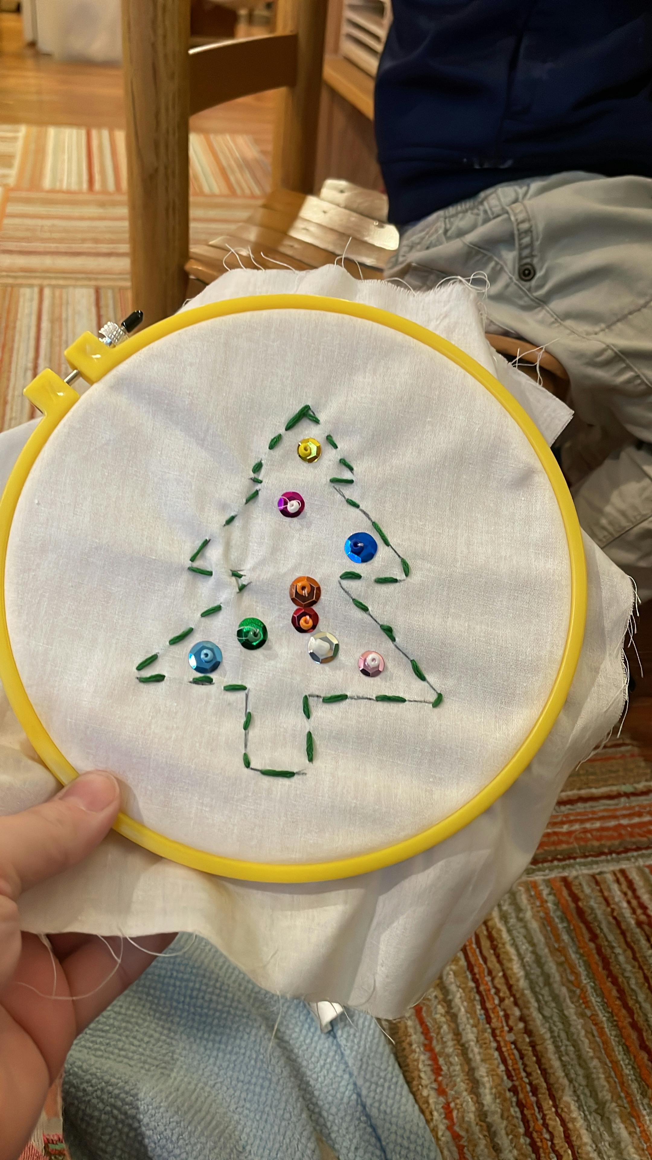 Person holding an embroidery hoop with a stitched Christmas tree design