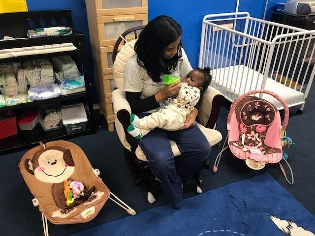 Person feeding a child with a bottle while sitting in a chair