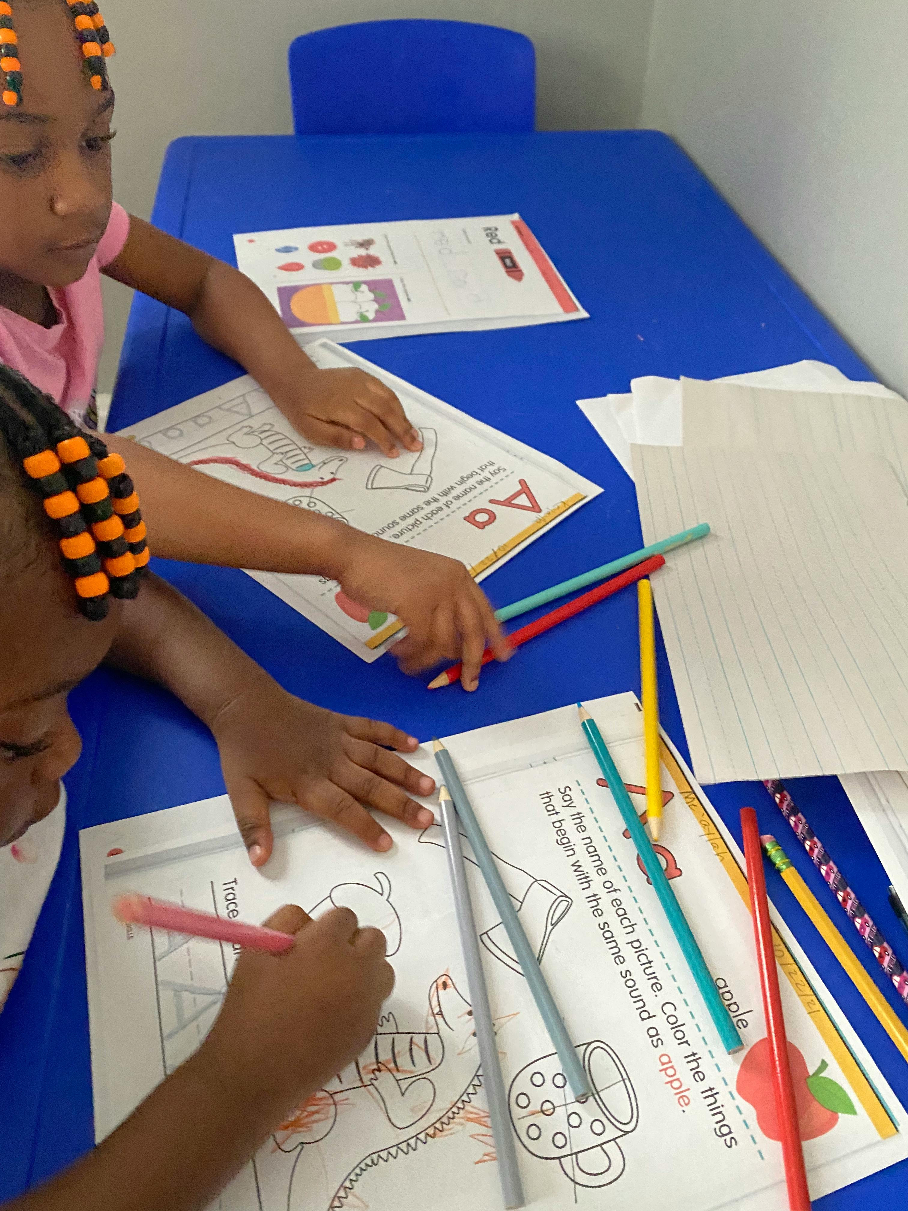 Two children coloring at a blue table with crayons and coloring pages