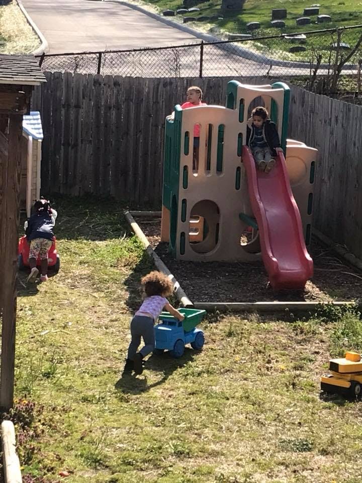 Children playing on a slide and with toy trucks in a grassy area