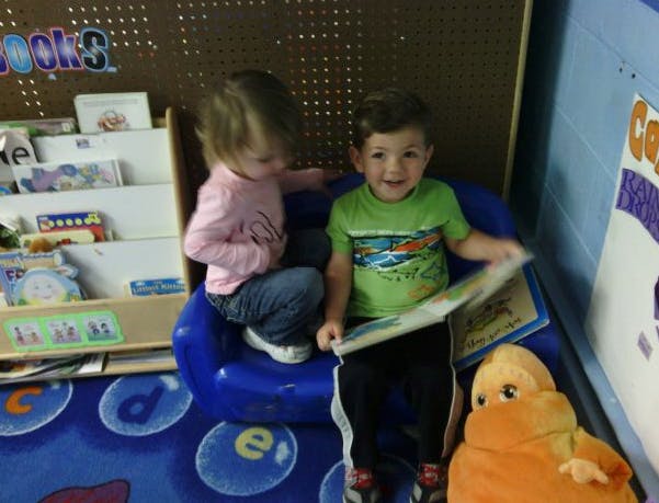 Two children sitting in a classroom, one holding a book