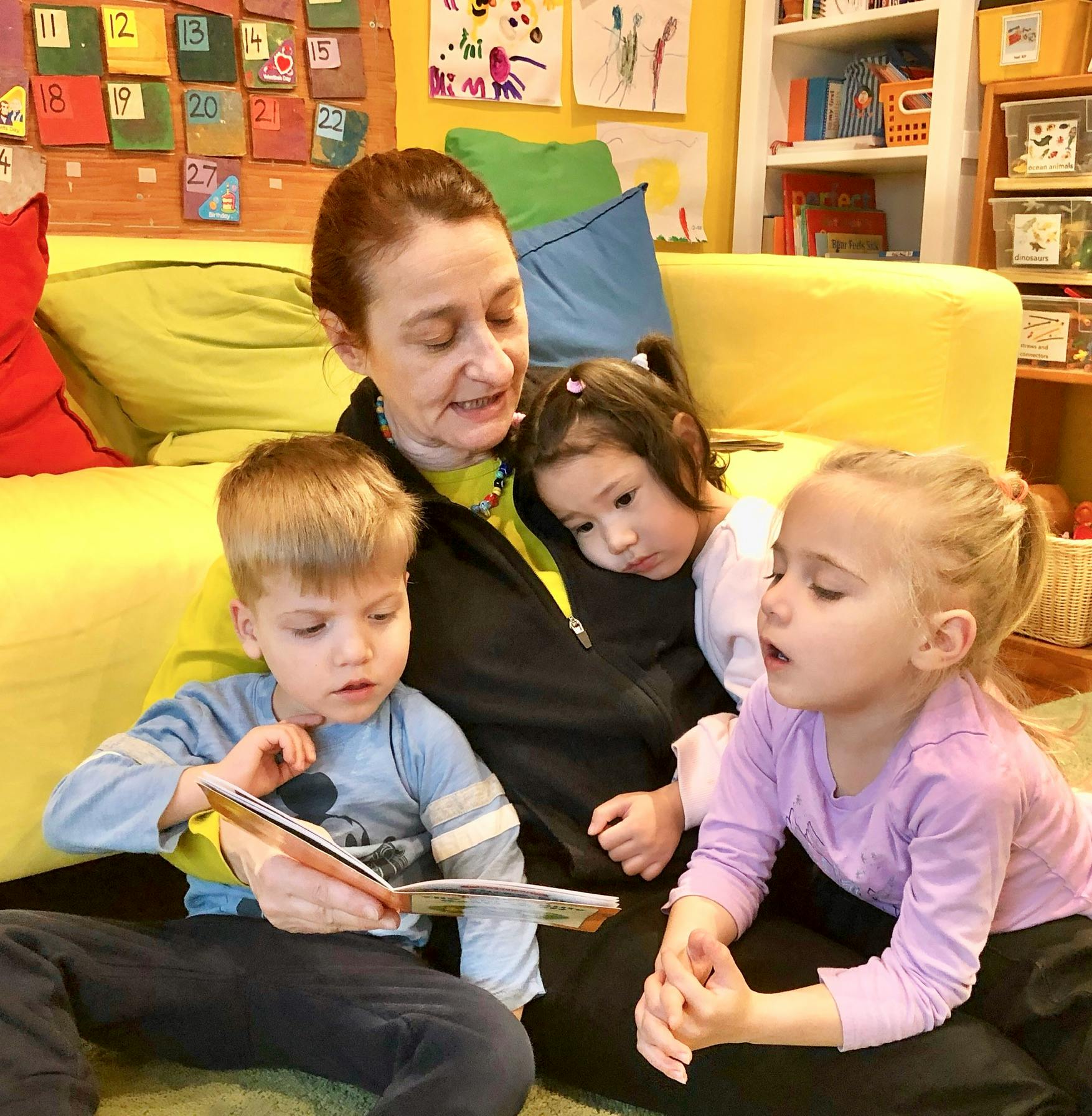 Person with three children, one child reading a book