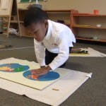 Child on floor working with puzzle pieces on a puzzle in-lay puzzle