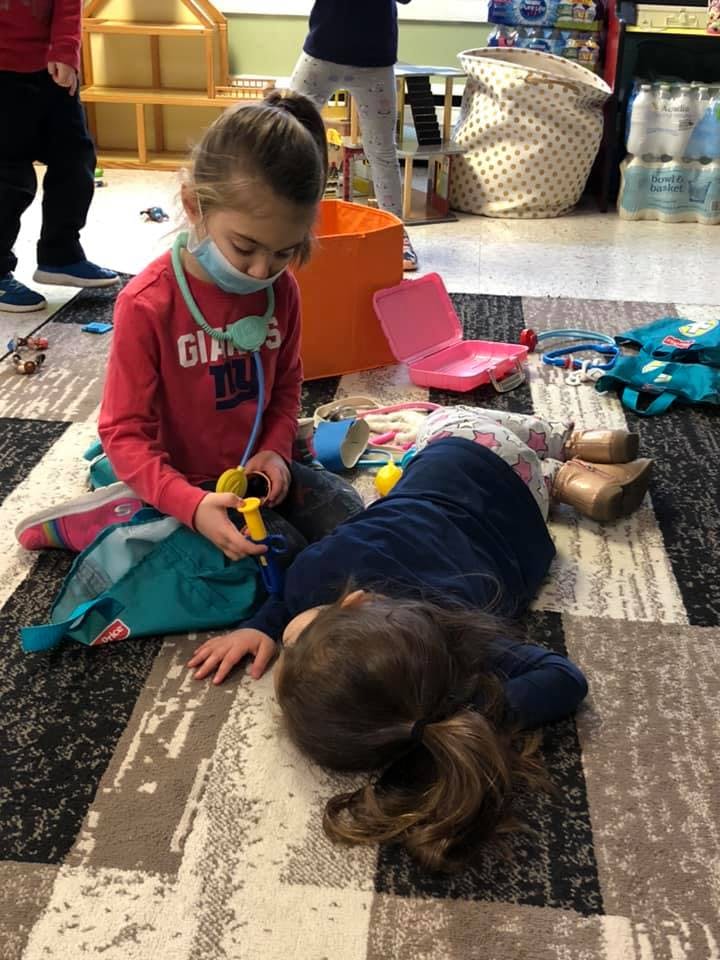 Child wearing a mask and stethoscope playing with another child on the floor