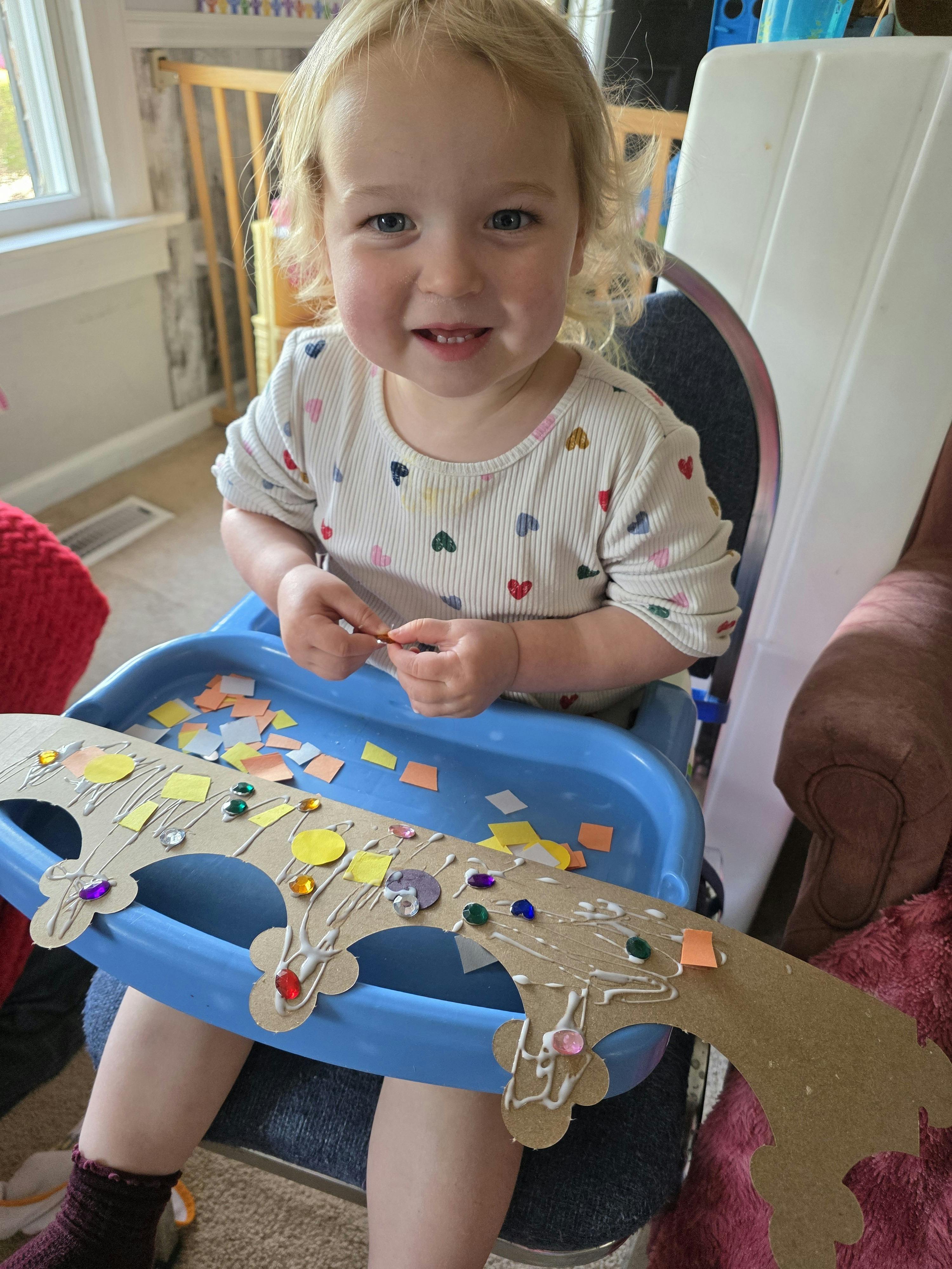 Child crafting with a paper crown and stickers in a high chair