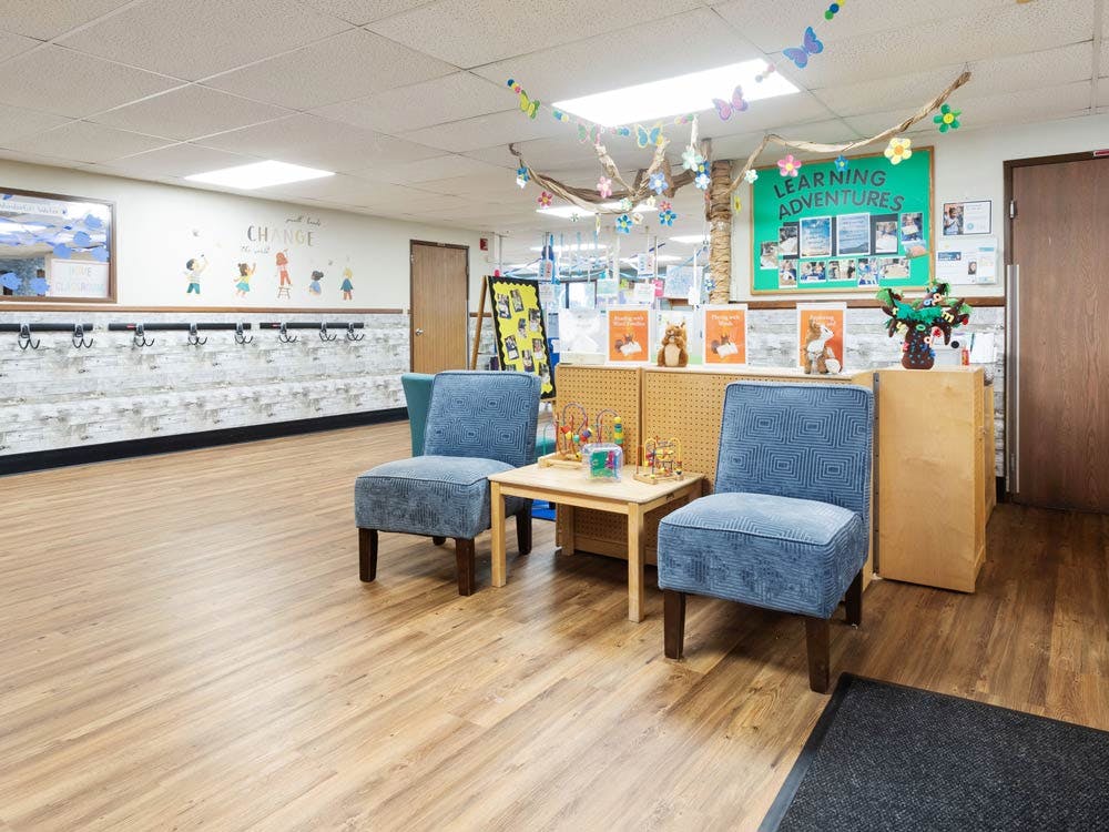 Classroom with child-sized furniture and a green board with "LEARNING ADVENTURES"